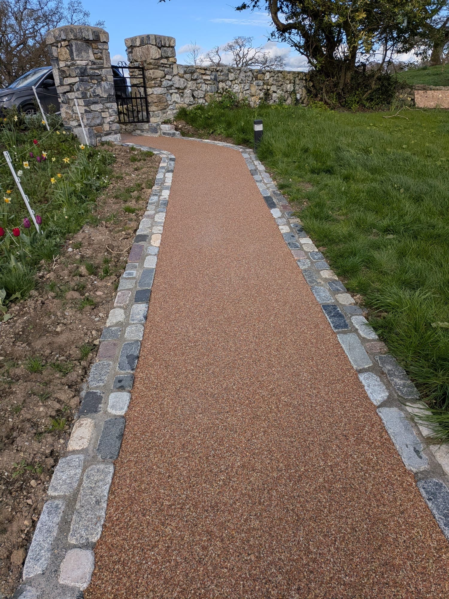 Curved Pathway with Granite Border — A sweeping terracotta-toned pathway finished with a natural granite setts border, leading to the gate.